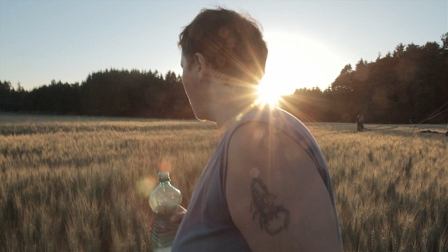 Filmstill aus "Nervenbruch Zusammen": eine Frau steht in eimem Feld im Sonnenlicht